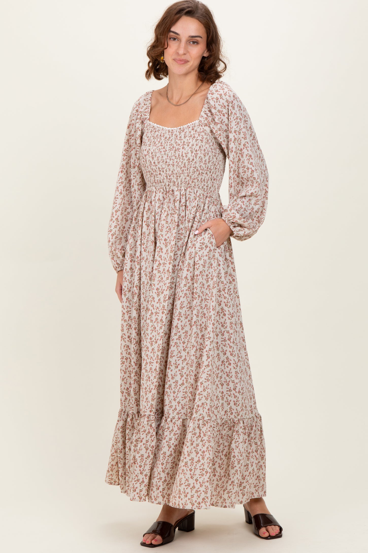woman wearing a cream floral maxi dress with long puff sleeves and pockets, standing against a neutral background