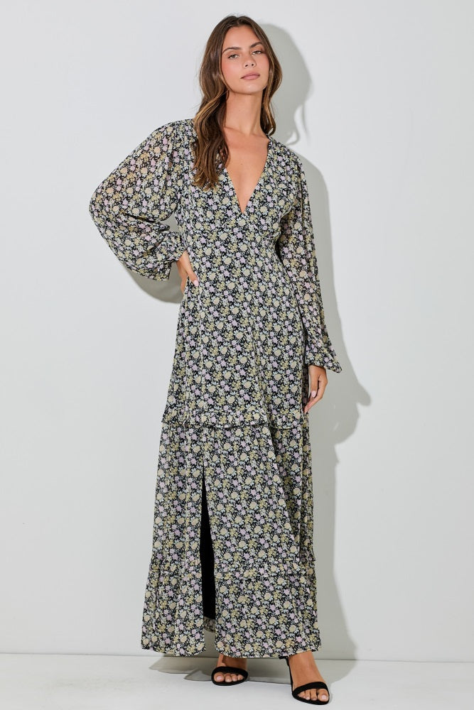 woman wearing a black floral maxi dress with a v-neckline, long sleeves, and a front slit.