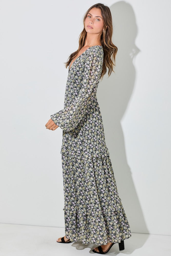 woman wearing a black floral maxi dress with long sleeves and tiered detailing, standing sideways against a plain background