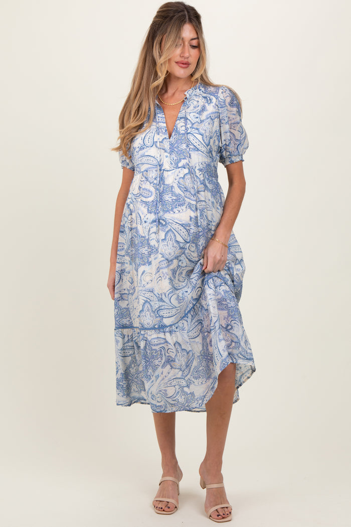 woman wearing a blue and white paisley print maternity dress with short sleeves and a tiered hem, showing her baby bump