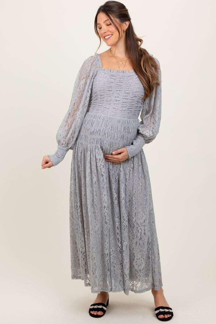 woman wearing a light gray lace maternity dress with long sleeves and a square neckline, holding her baby bump