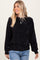 woman wearing a black ribbed pullover sweater with long sleeves and a relaxed fit, paired with denim jeans