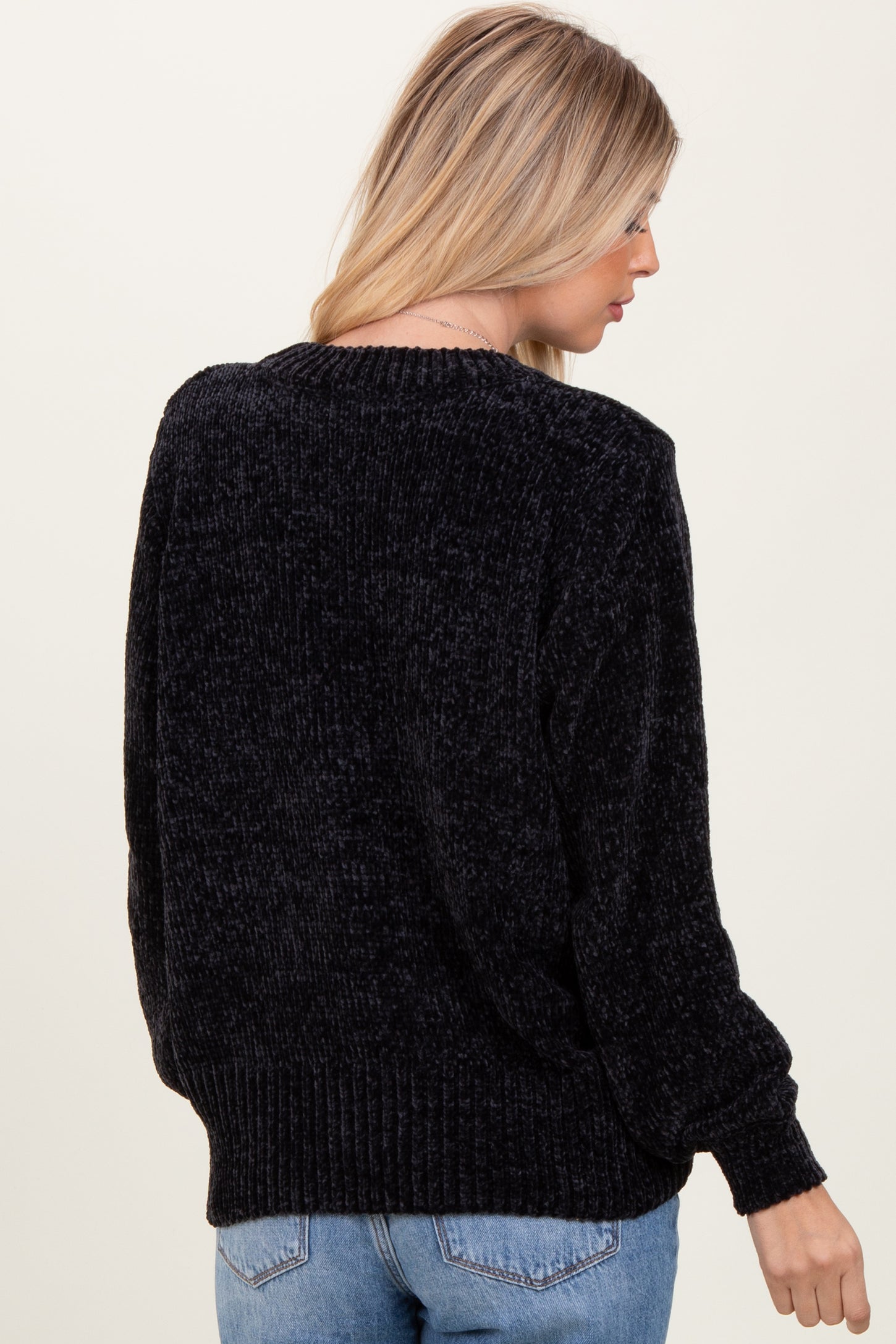 woman wearing a cozy black oversized sweater with a ribbed hem and slightly puffed sleeves, viewed from the back