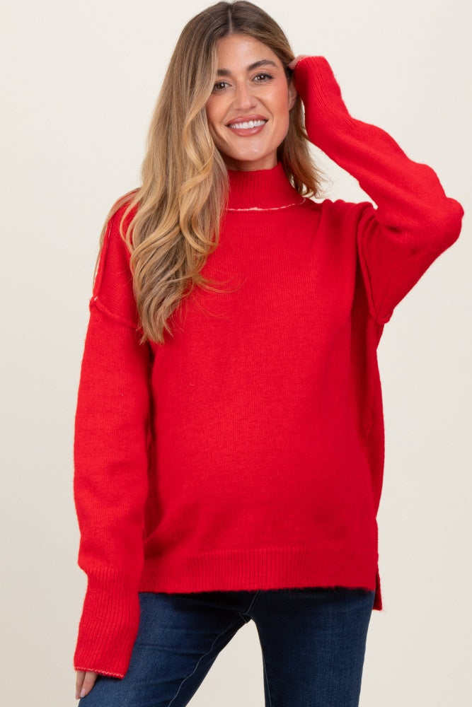 woman wearing a red turtleneck maternity sweater and blue jeans, smiling and touching her hair