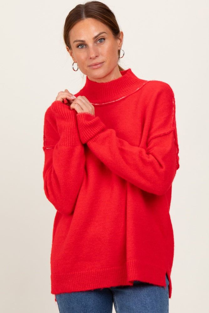 woman wearing a bright red oversized turtleneck sweater with side slits and long sleeves