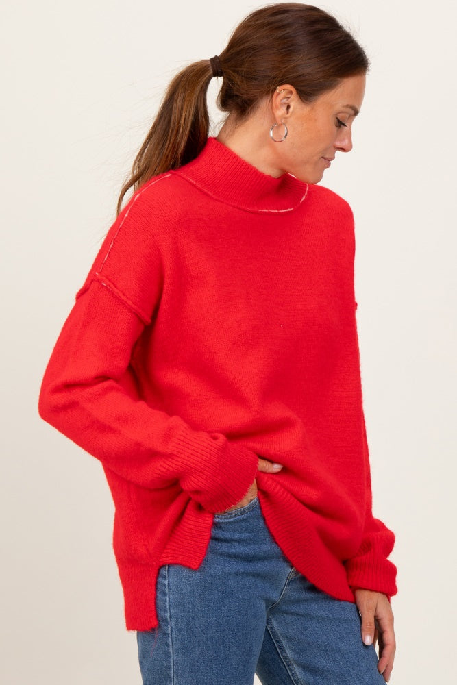 woman wearing a red oversized turtleneck sweater with side slits and detail stitching, paired with blue jeans