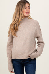 woman wearing a light beige long sleeve maternity sweater with a high neckline and relaxed fit, showing her baby bump