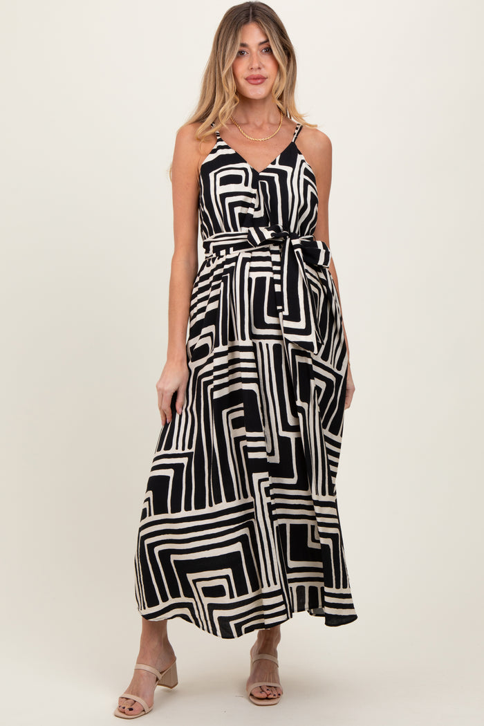 woman wearing a black and white geometric print maternity maxi dress with a tie waist and adjustable straps