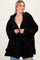 woman wearing a black plush hooded cardigan, smiling and holding it open over a beige top