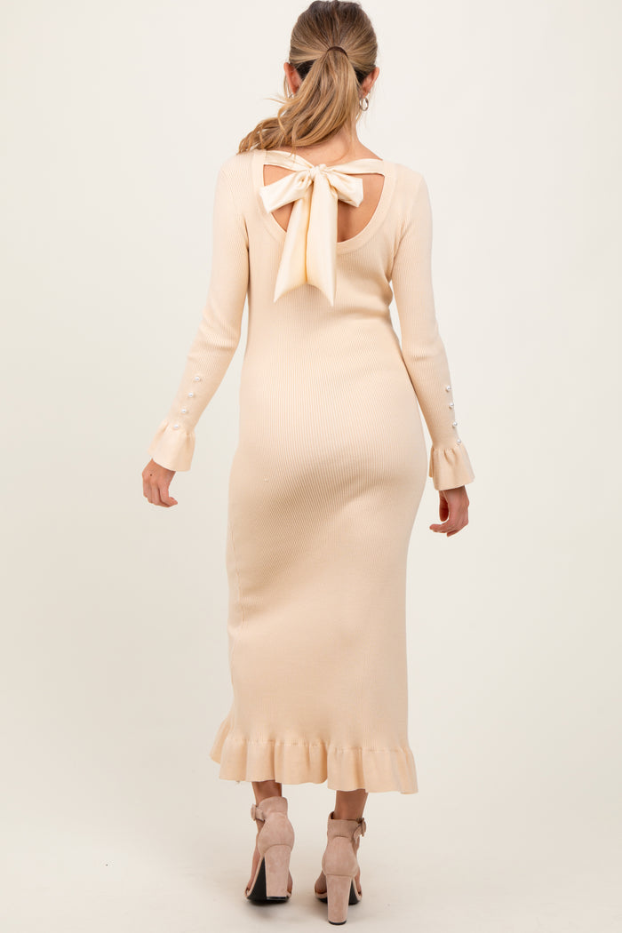 woman wearing a light beige ribbed maternity dress with a bow detail at the back and ruffle hem