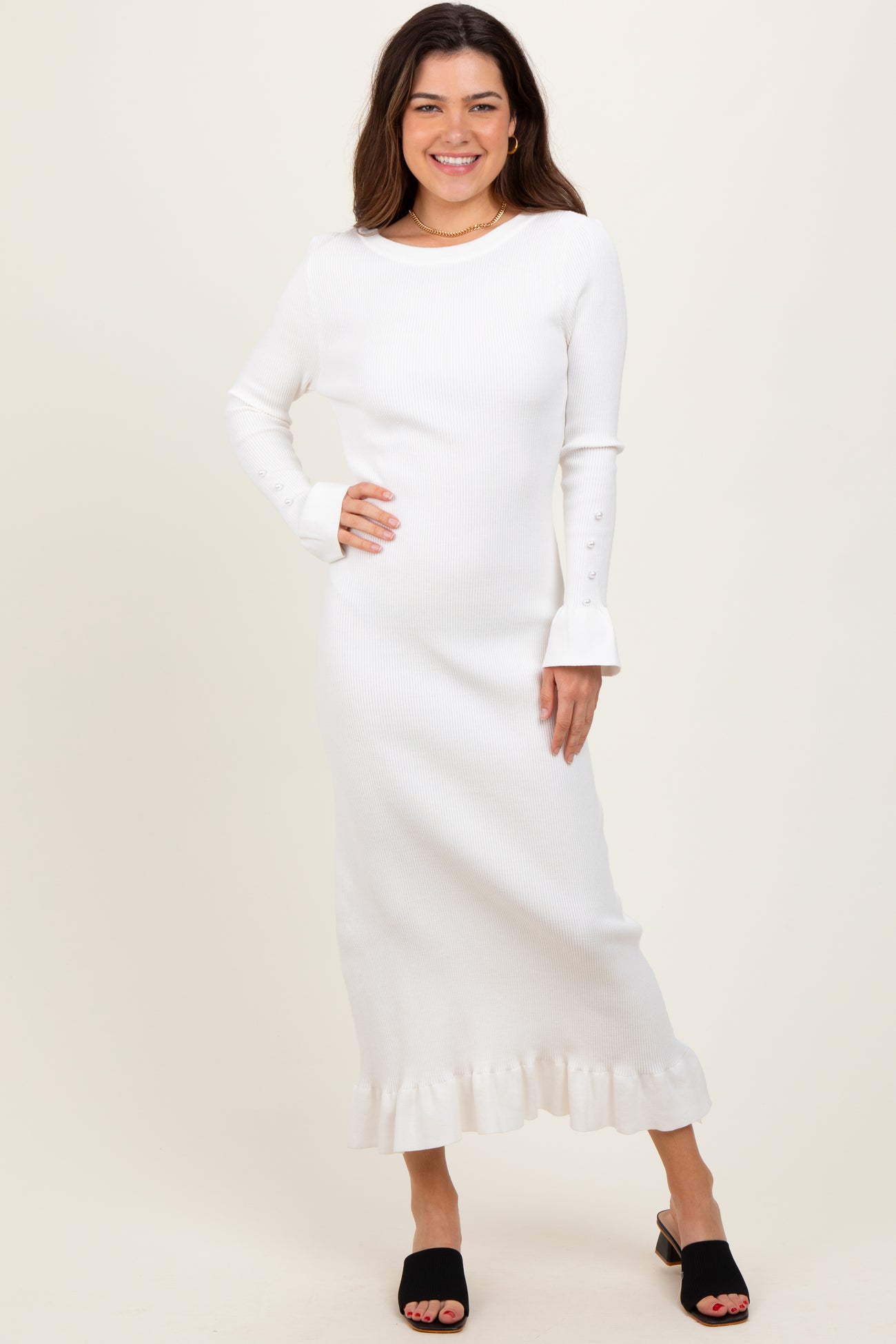 woman wearing a white ribbed long sleeve dress with flared cuffs and a ruffled hemline, styled with black slide sandals