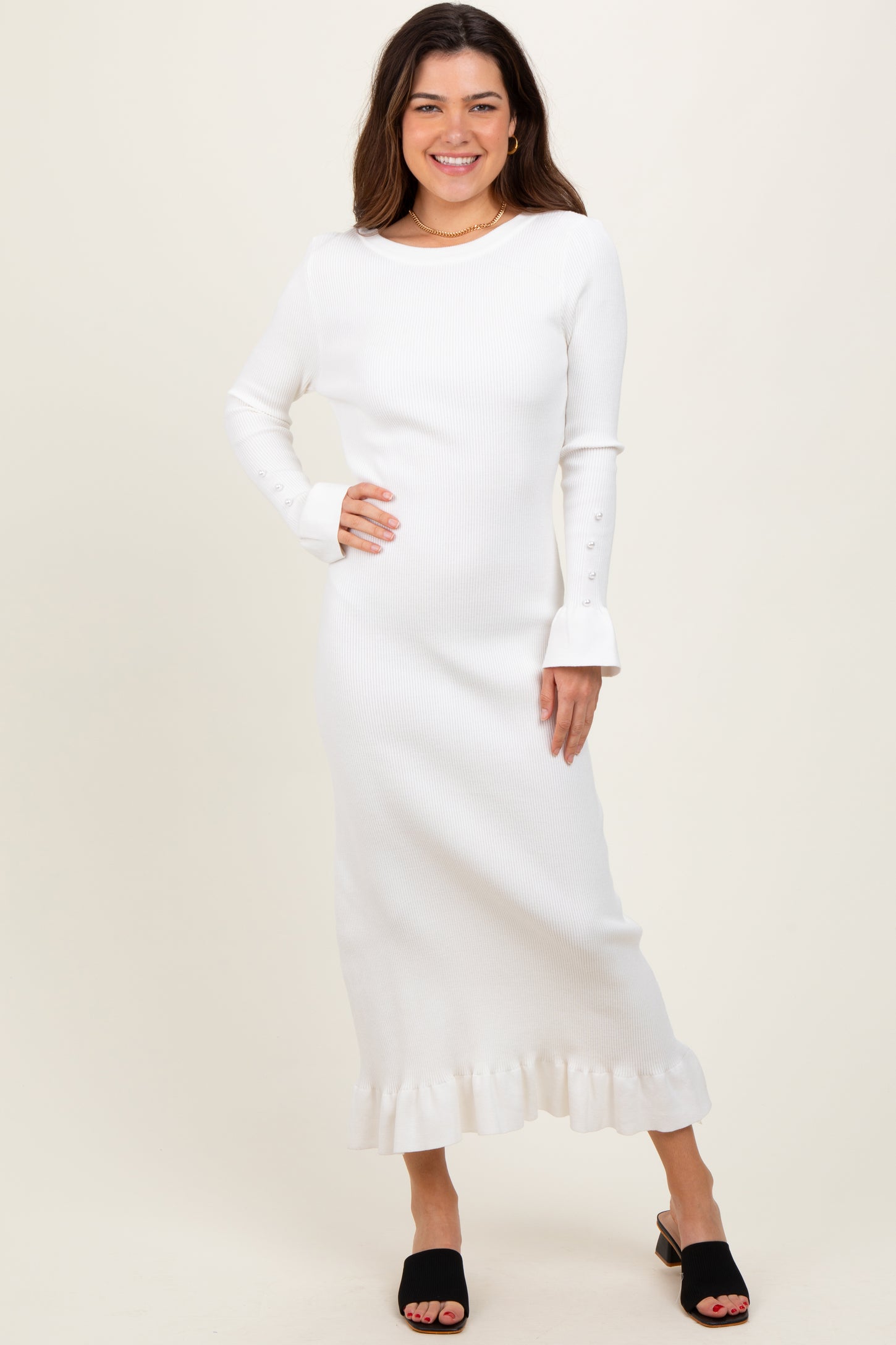 woman wearing a white ribbed long sleeve dress with flared cuffs and a ruffled hemline, styled with black slide sandals