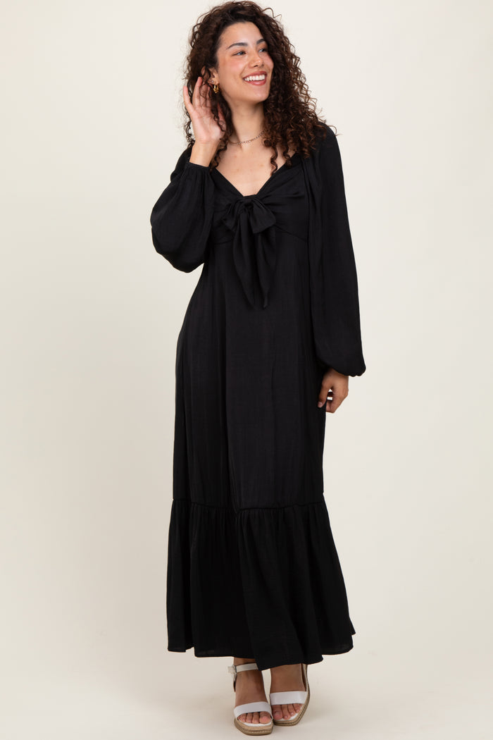 woman wearing a black maxi dress with a tie front and balloon sleeves, standing and smiling