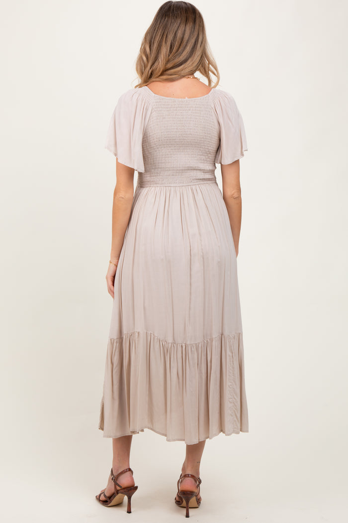 woman wearing a beige maternity dress with a smocked bodice and flutter sleeves, showcasing a flowy skirt