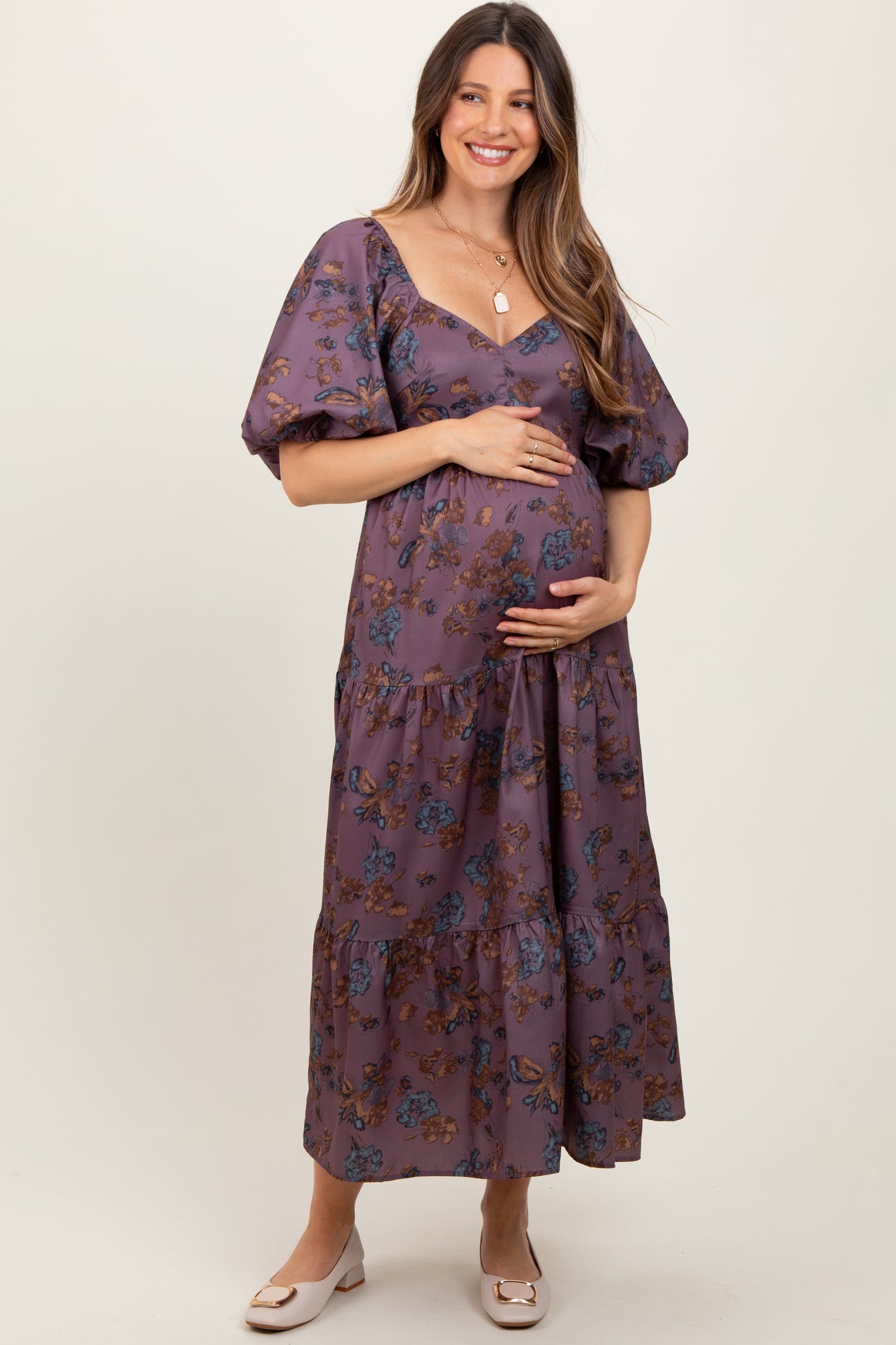 woman wearing a purple floral print maternity maxi dress and holding her baby bump