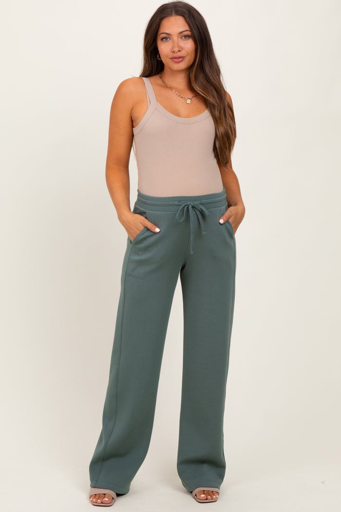 woman wearing a beige ribbed maternity bodysuit and green maternity sweatpants with pockets and a drawstring waist