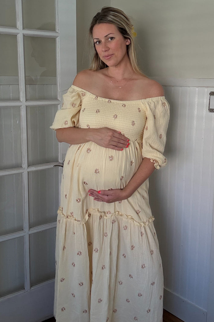 woman wearing a yellow floral off-the-shoulder maternity dress and holding her baby bump