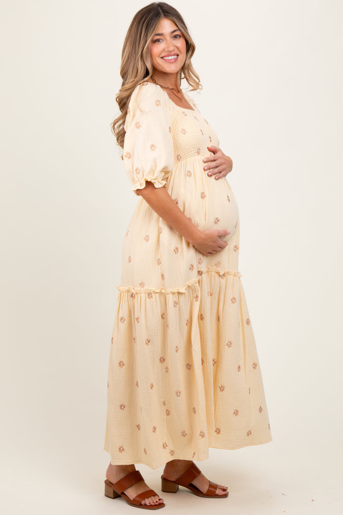 woman wearing a cream floral maternity dress with puff sleeves and a tiered skirt, cradling her baby bump