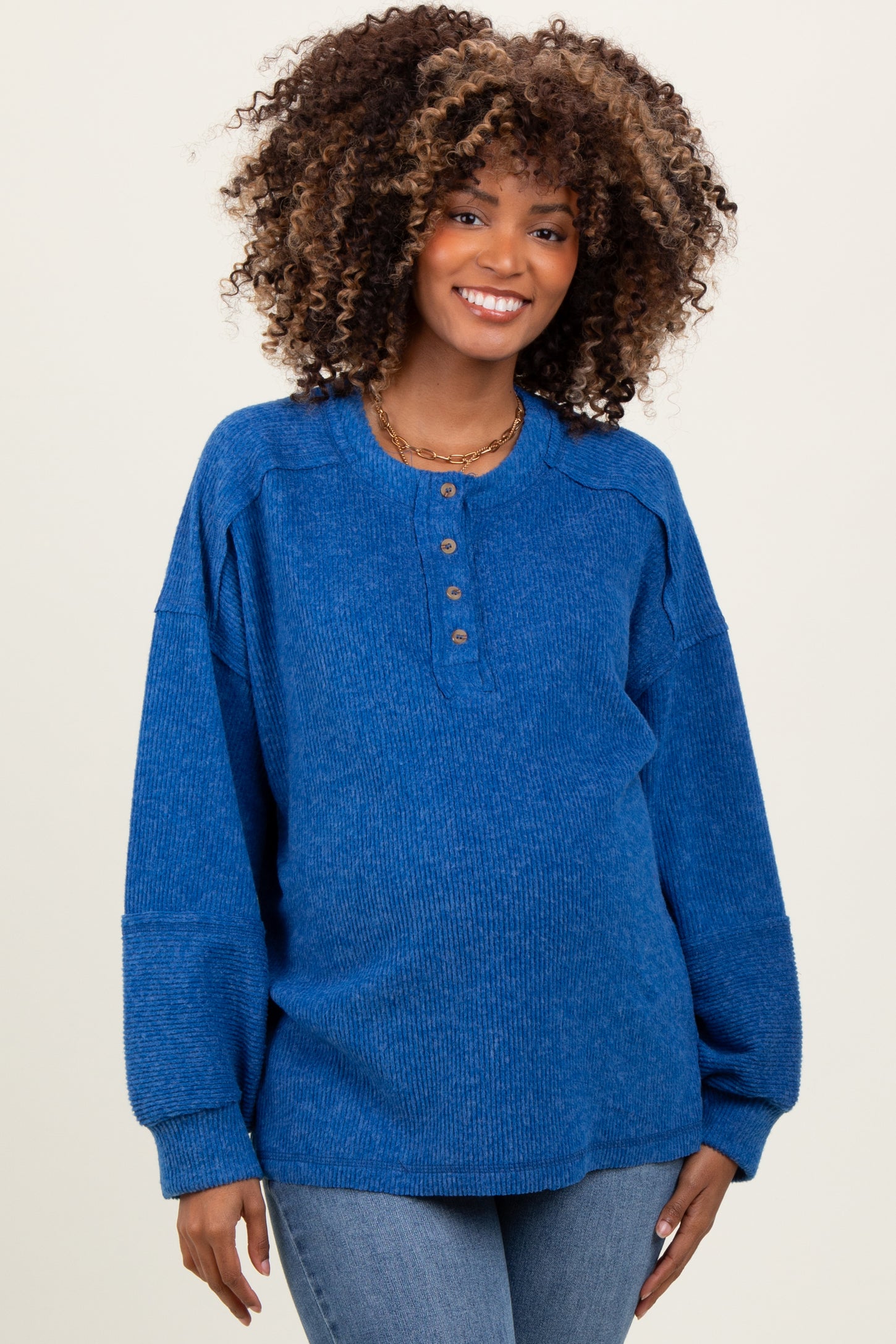 woman wearing a blue ribbed maternity top with button details and long sleeves, smiling at the camera