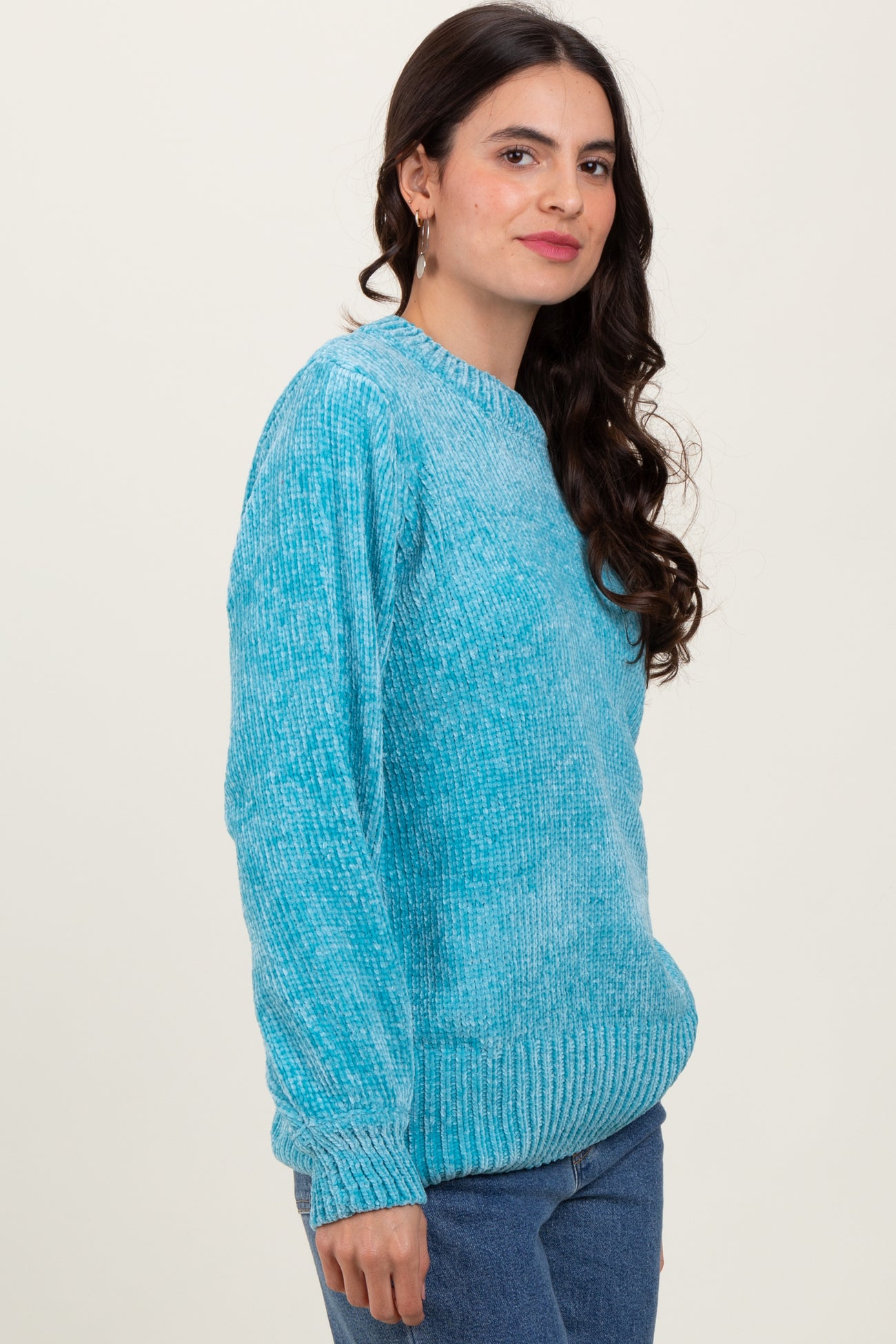 woman wearing an aqua blue oversized knit sweater with long sleeves and ribbed hem, standing sideways against a neutral background