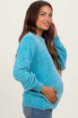woman wearing a turquoise maternity sweater with long sleeves and a relaxed fit, gently cradling her baby bump