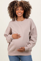 woman wearing a taupe oversized sweatshirt, holding her baby bump, maternity wear, styled with blue jeans