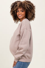 woman wearing a taupe maternity sweatshirt with a visible baby bump and blue jeans