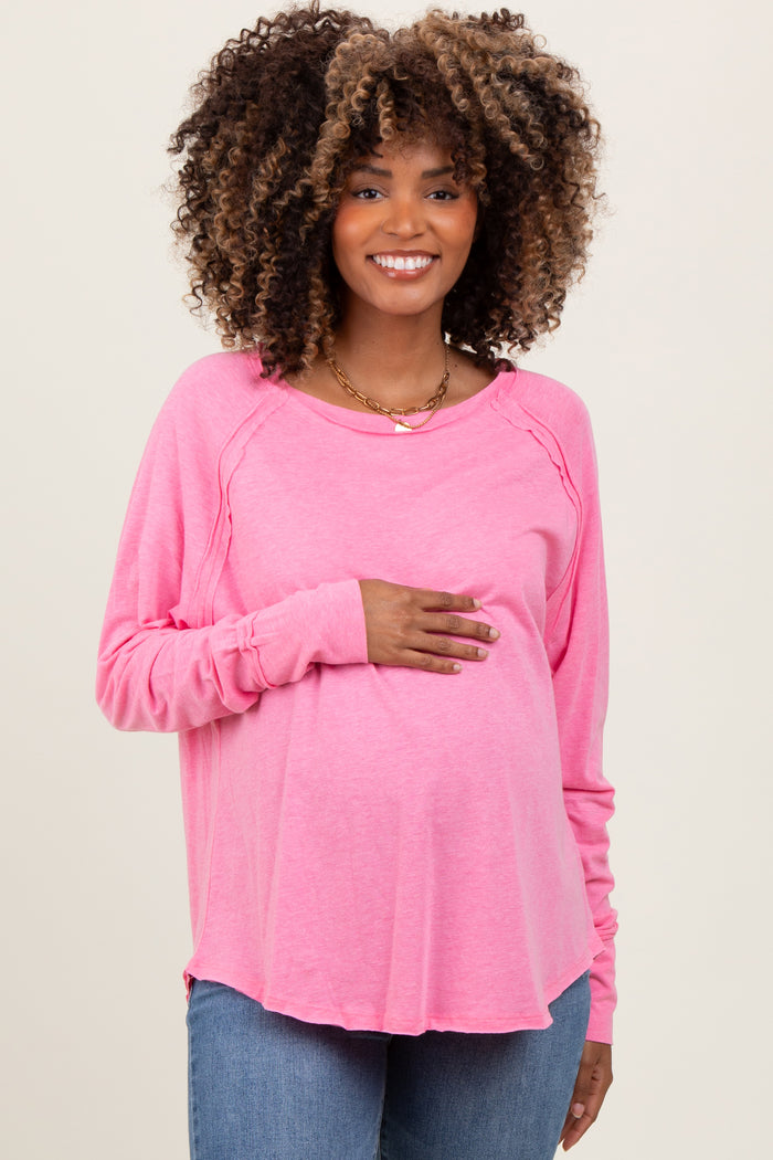 woman wearing a pink long sleeve maternity top and holding her baby bump