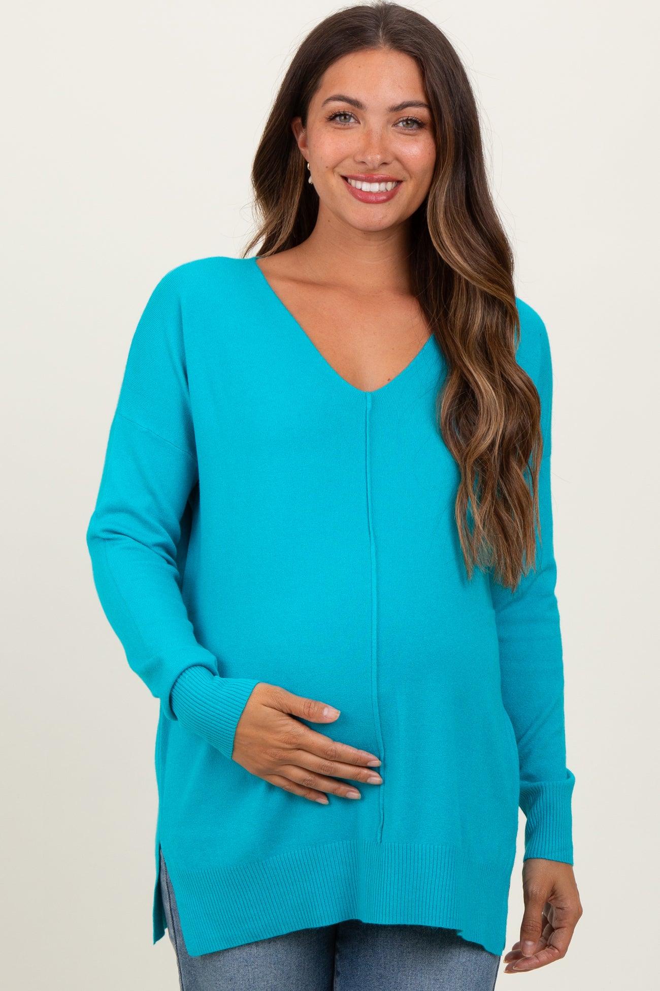 woman wearing a vibrant turquoise maternity sweater with a deep v-neck and side slits, cradling her baby bump