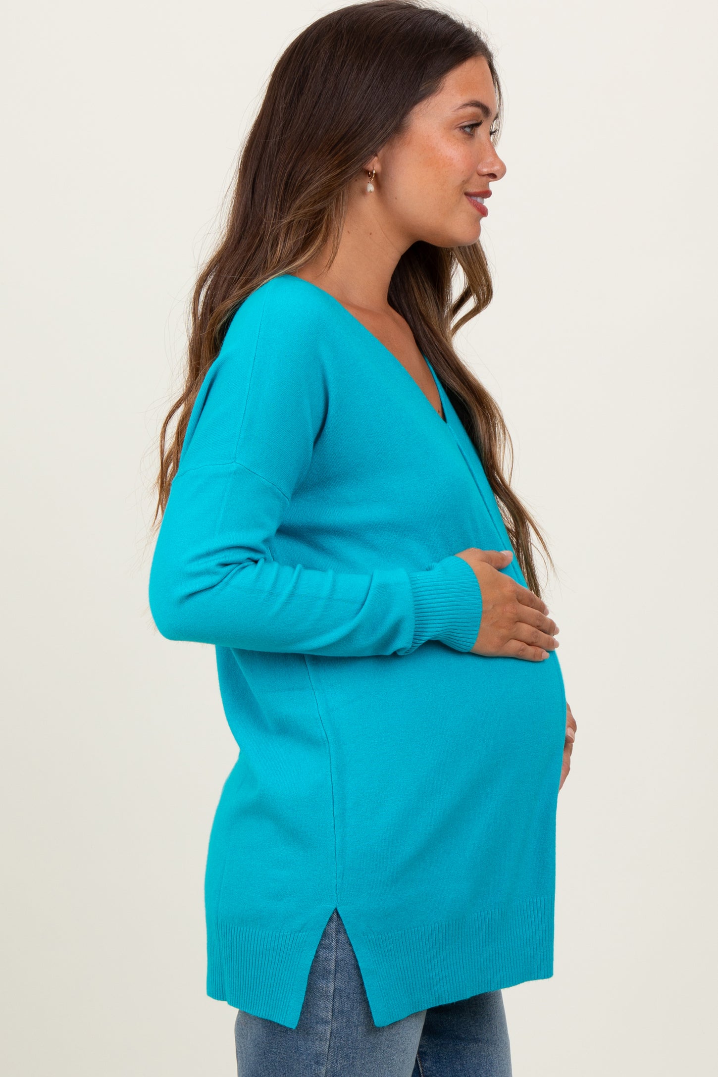 woman wearing a teal maternity sweater with a v-neck and side slits, highlighting her baby bump