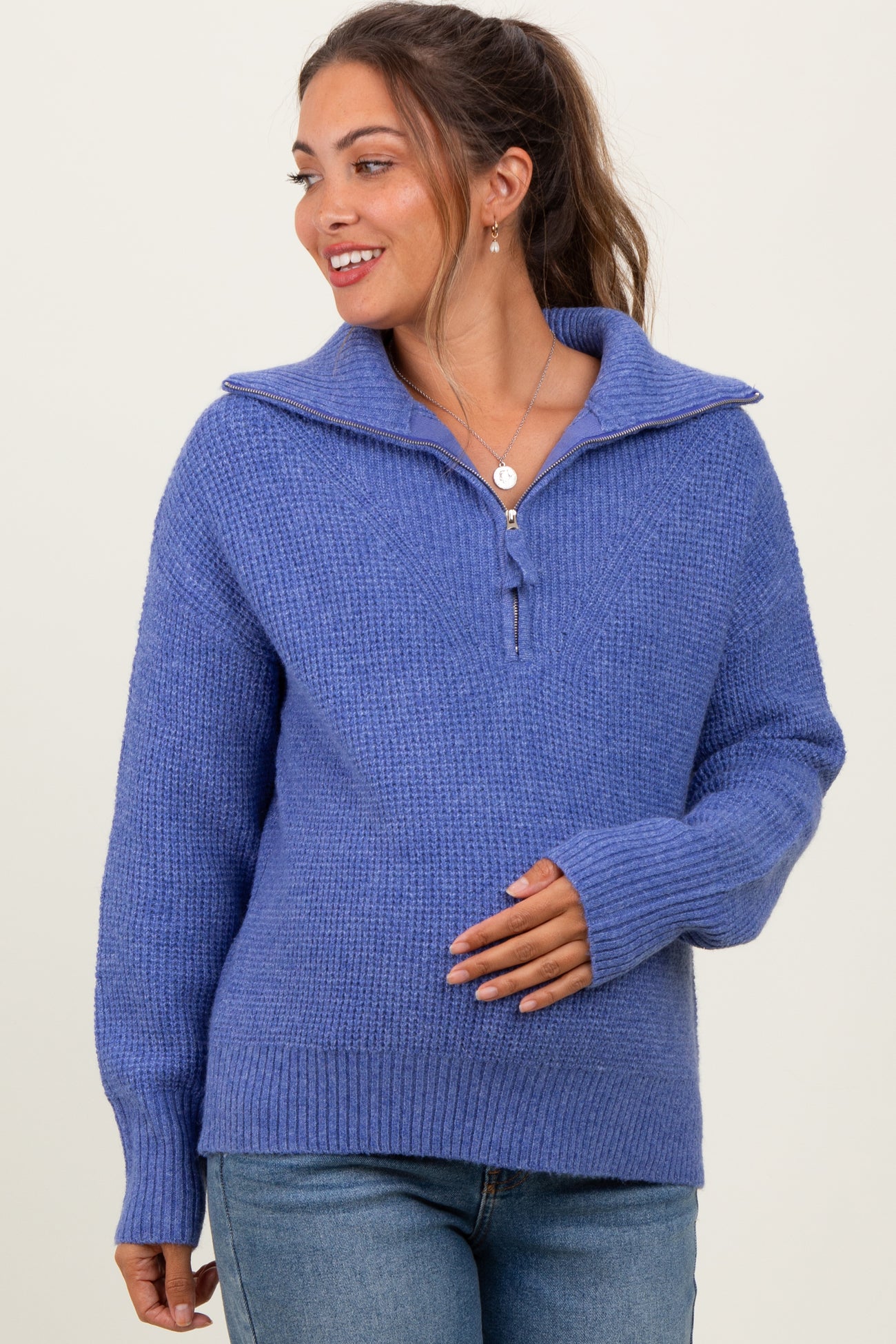woman wearing a purple maternity sweater with a zip collar and a relaxed fit, gently cradling her baby bump