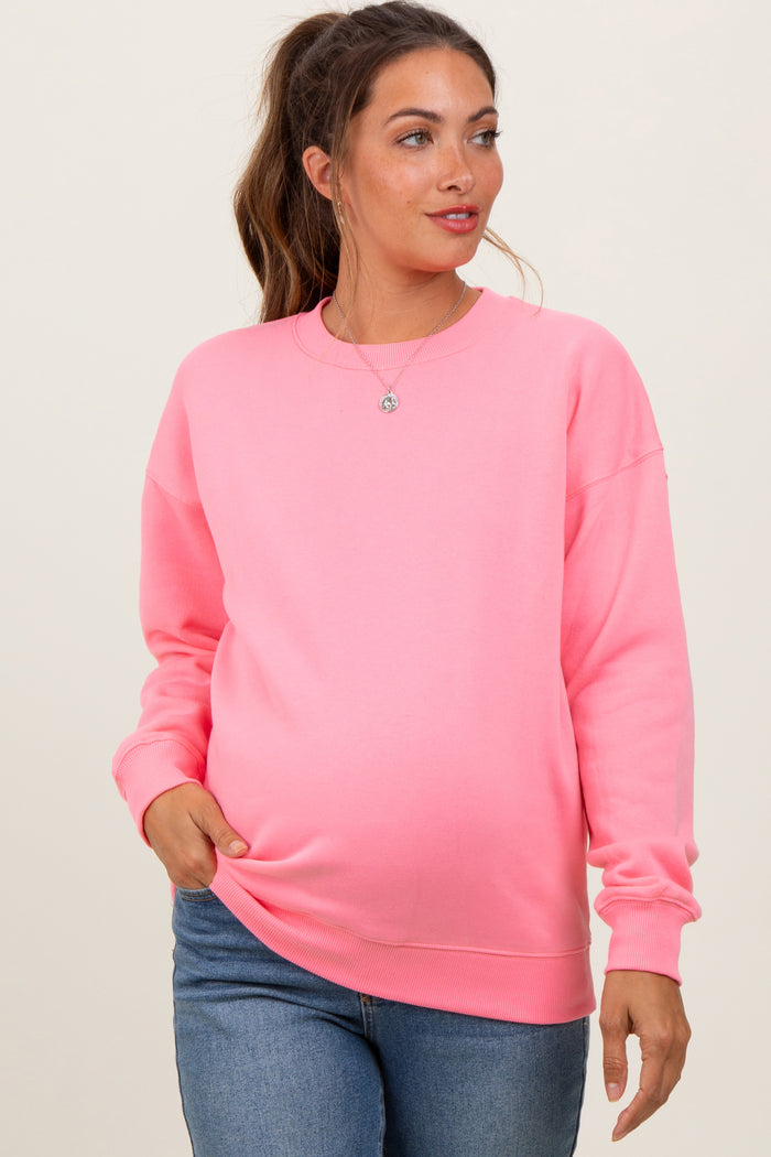 woman wearing a bright pink maternity sweatshirt and showing her baby bump while smiling