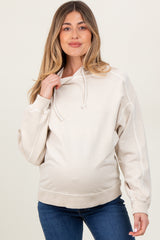 woman wearing a cream maternity hoodie with a relaxed fit and drawstring hood, showcasing a visible baby bump