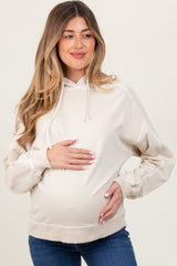 woman wearing a beige maternity hoodie and holding her baby bump