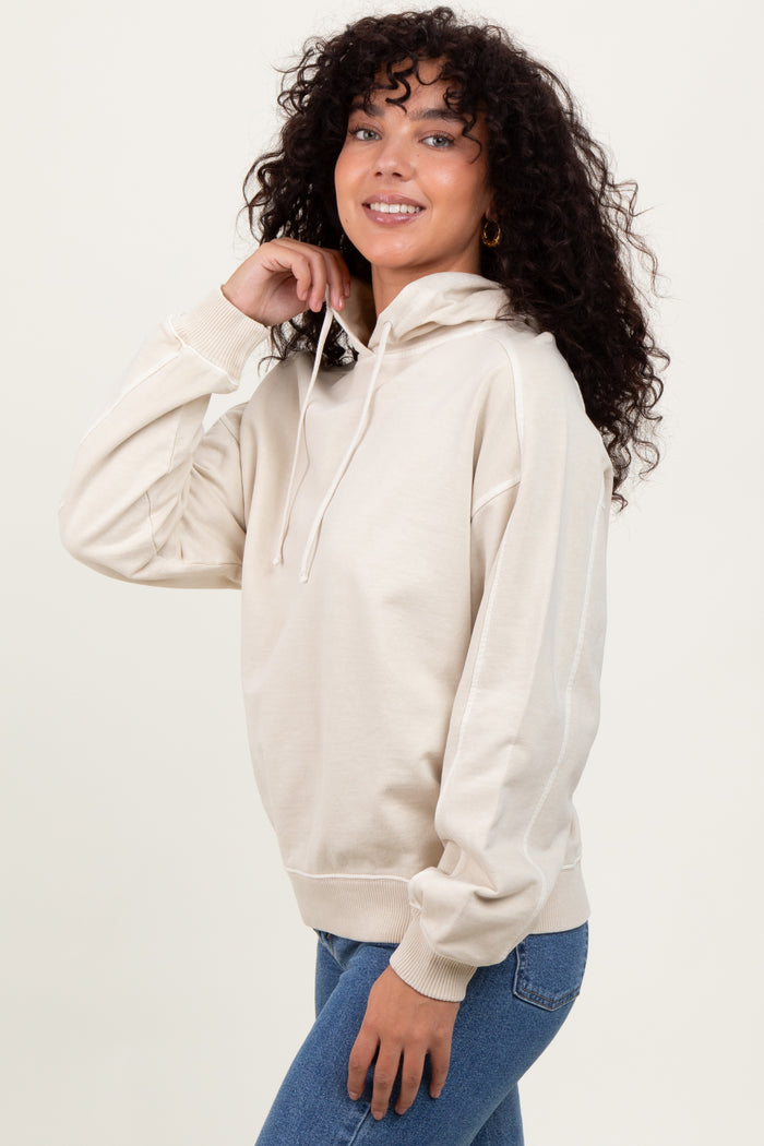 woman wearing a beige hooded sweatshirt with a relaxed fit and long sleeves, styled with blue jeans