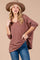 woman wearing a oversized mauve long sleeve sweater with a v-neck and distressed jeans, accessorized with a wide-brim hat