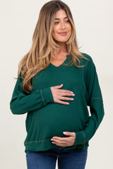 woman wearing a dark green maternity long sleeve top, smiling and holding her baby bump