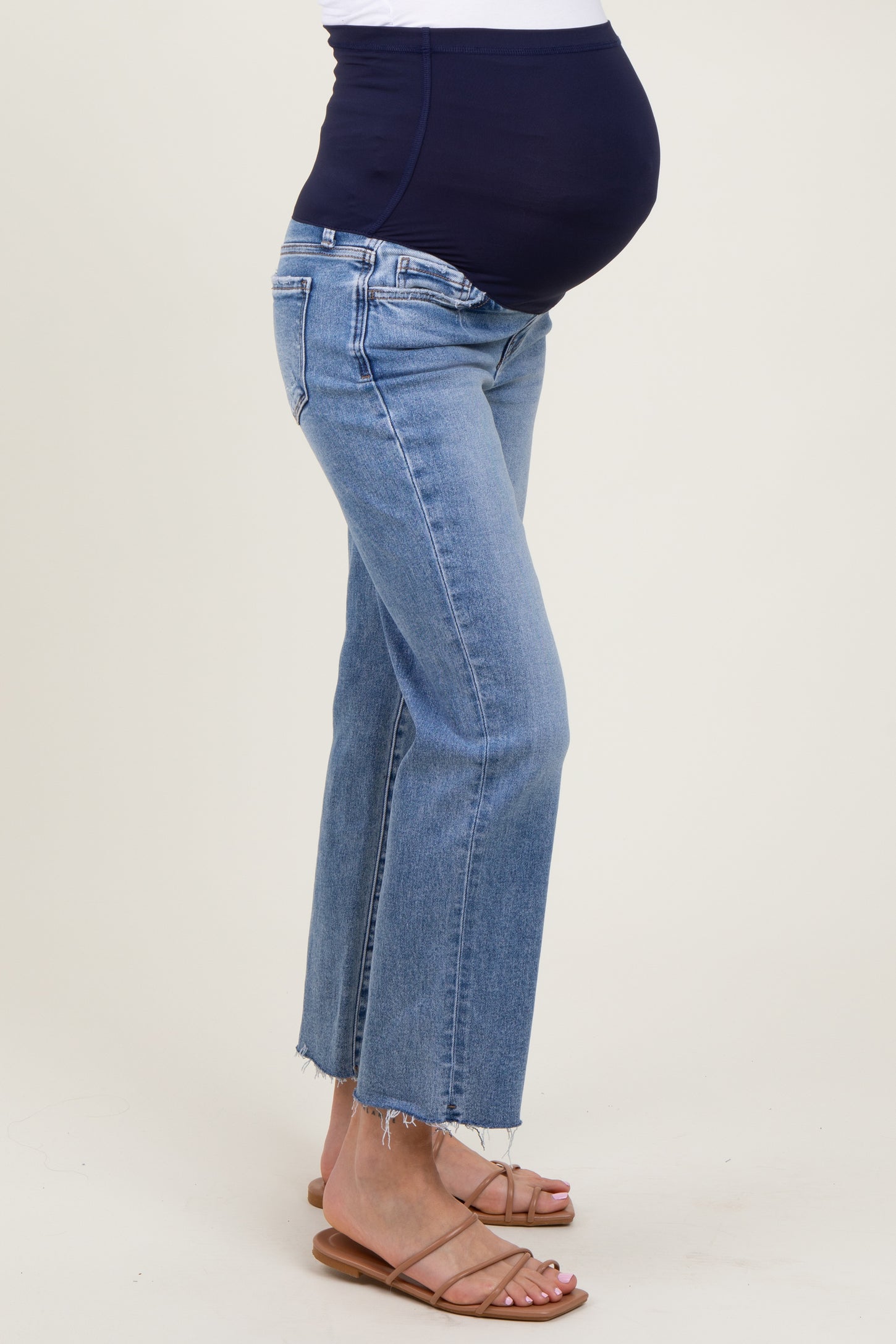 woman wearing light blue maternity cropped jeans with a dark navy belly panel and a visible baby bump