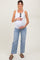 woman wearing a white tank top and light blue jeans, showing her baby bump while holding it gently