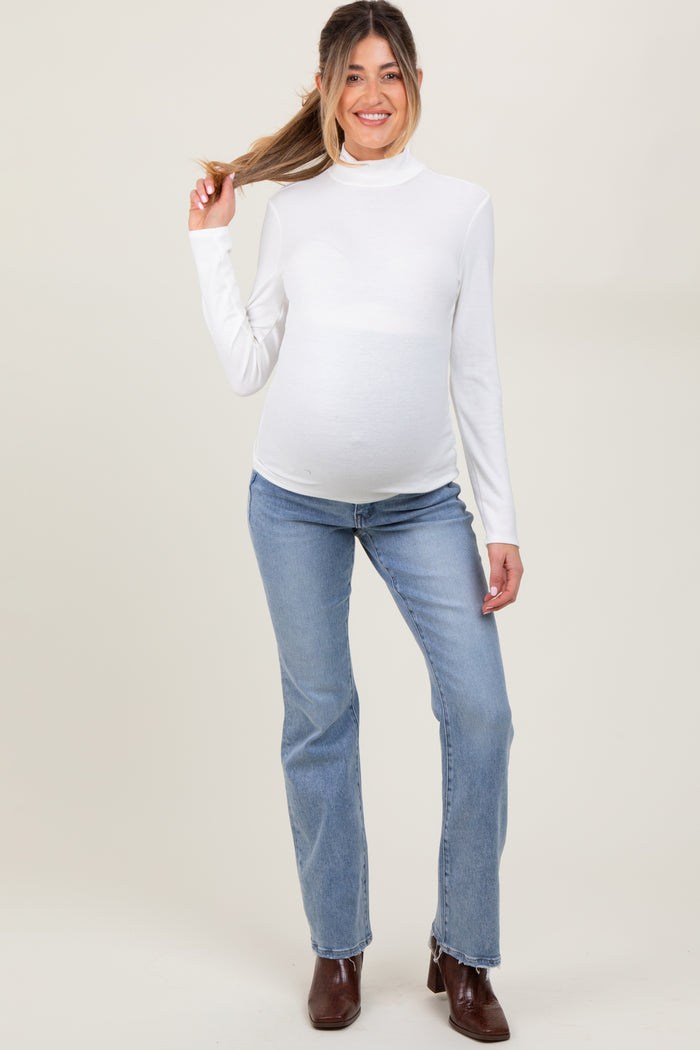 woman wearing a white long sleeve maternity top and blue jeans, showing her baby bump while posing with her hair