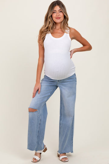 woman wearing a white maternity tank top and distressed light blue jeans, showing her baby bump