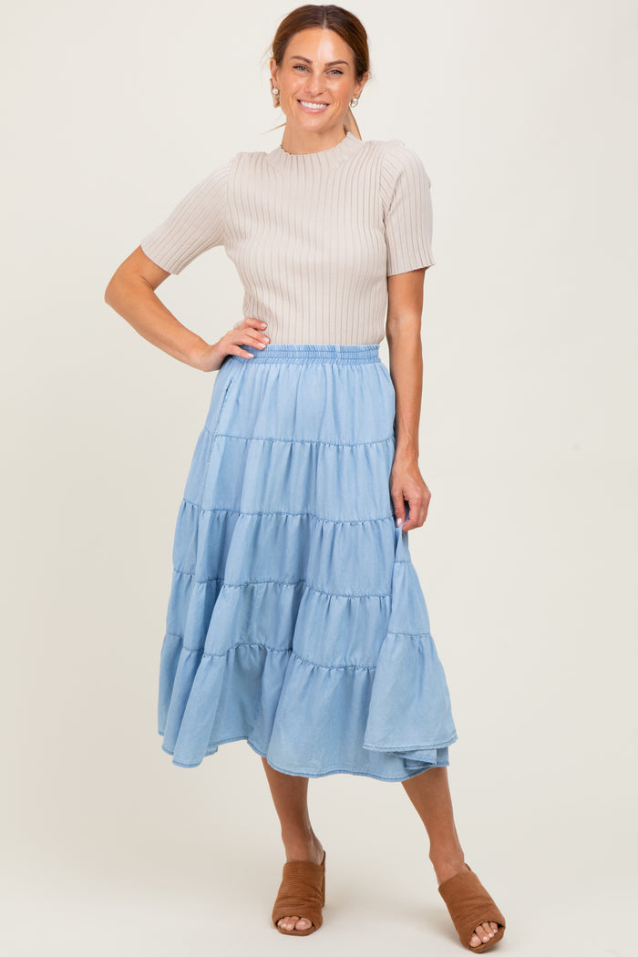 woman wearing a beige ribbed short sleeve top and a tiered light blue maxi skirt with brown heeled sandals