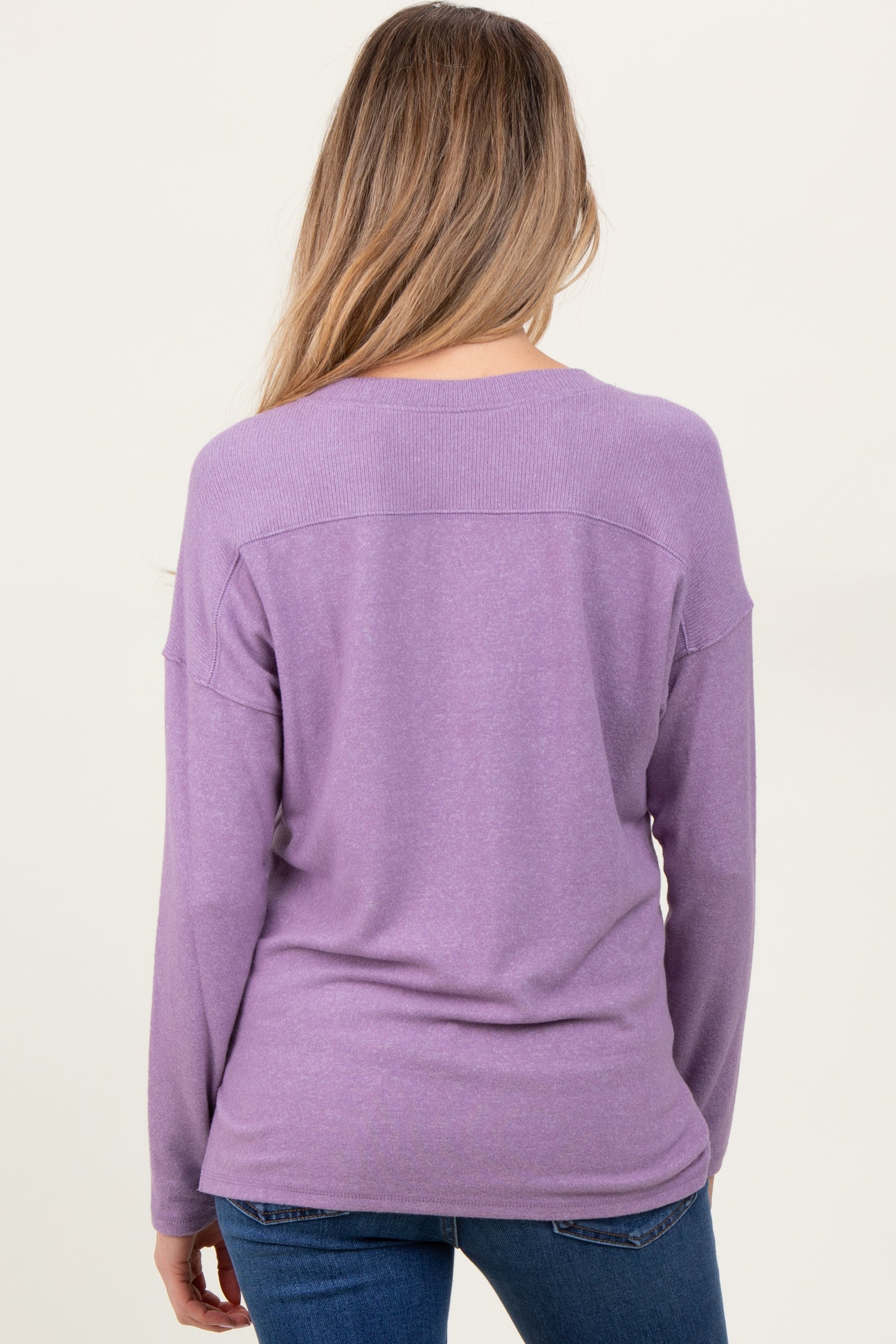 woman wearing a purple long sleeve maternity top, viewed from the back, paired with blue jeans