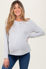 woman wearing a light gray maternity top with button details and a visible baby bump