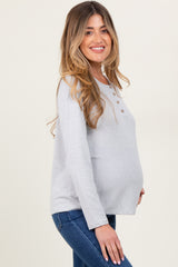 woman wearing a light gray maternity long sleeve top with button details and visible baby bump