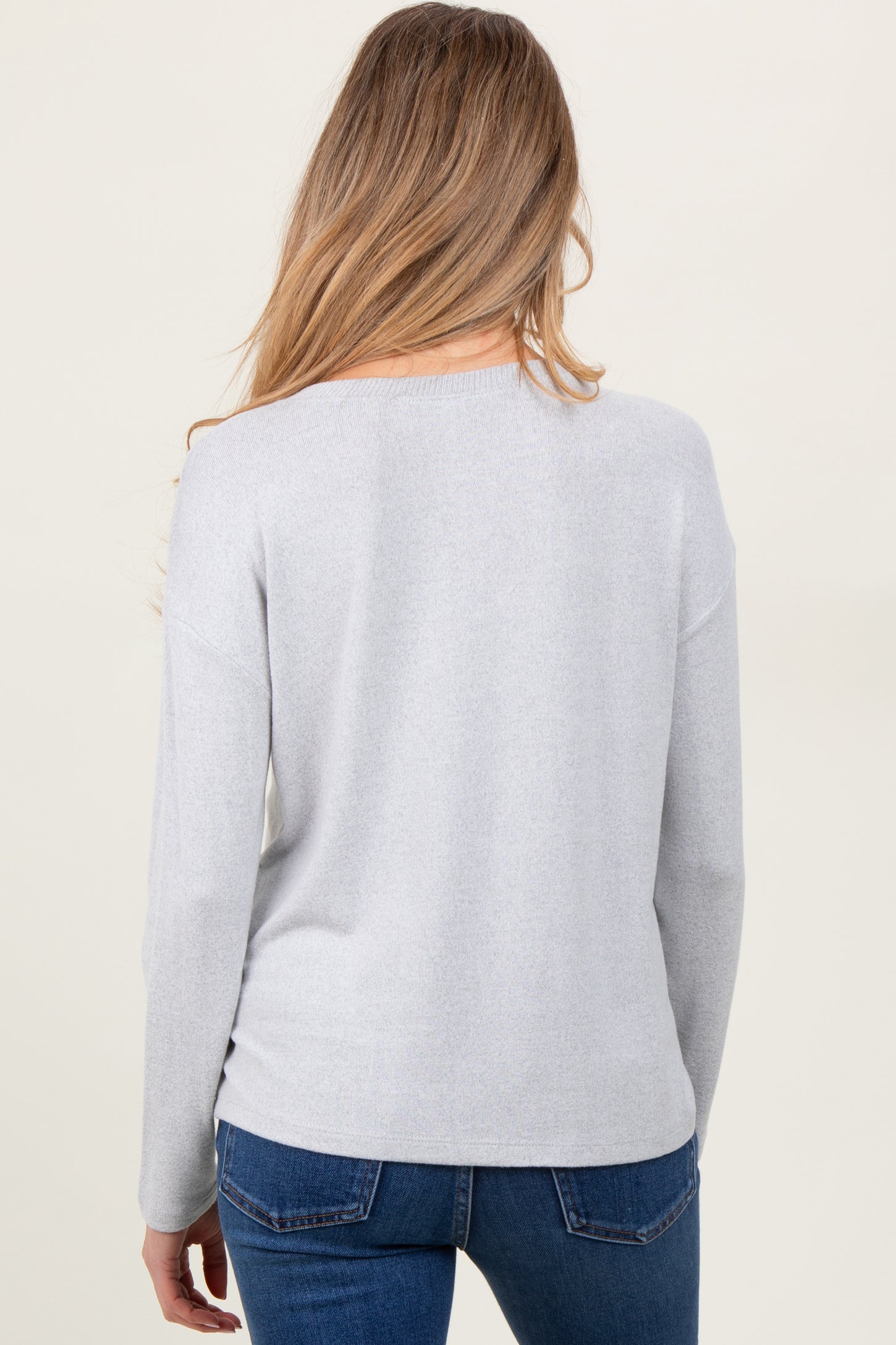 woman wearing a light gray maternity pullover sweater, viewed from the back, paired with blue jeans