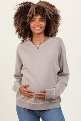woman wearing a light gray maternity sweatshirt and holding her baby bump