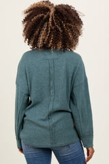 woman wearing a teal maternity sweater with a relaxed fit and back seam detail, styled with blue jeans