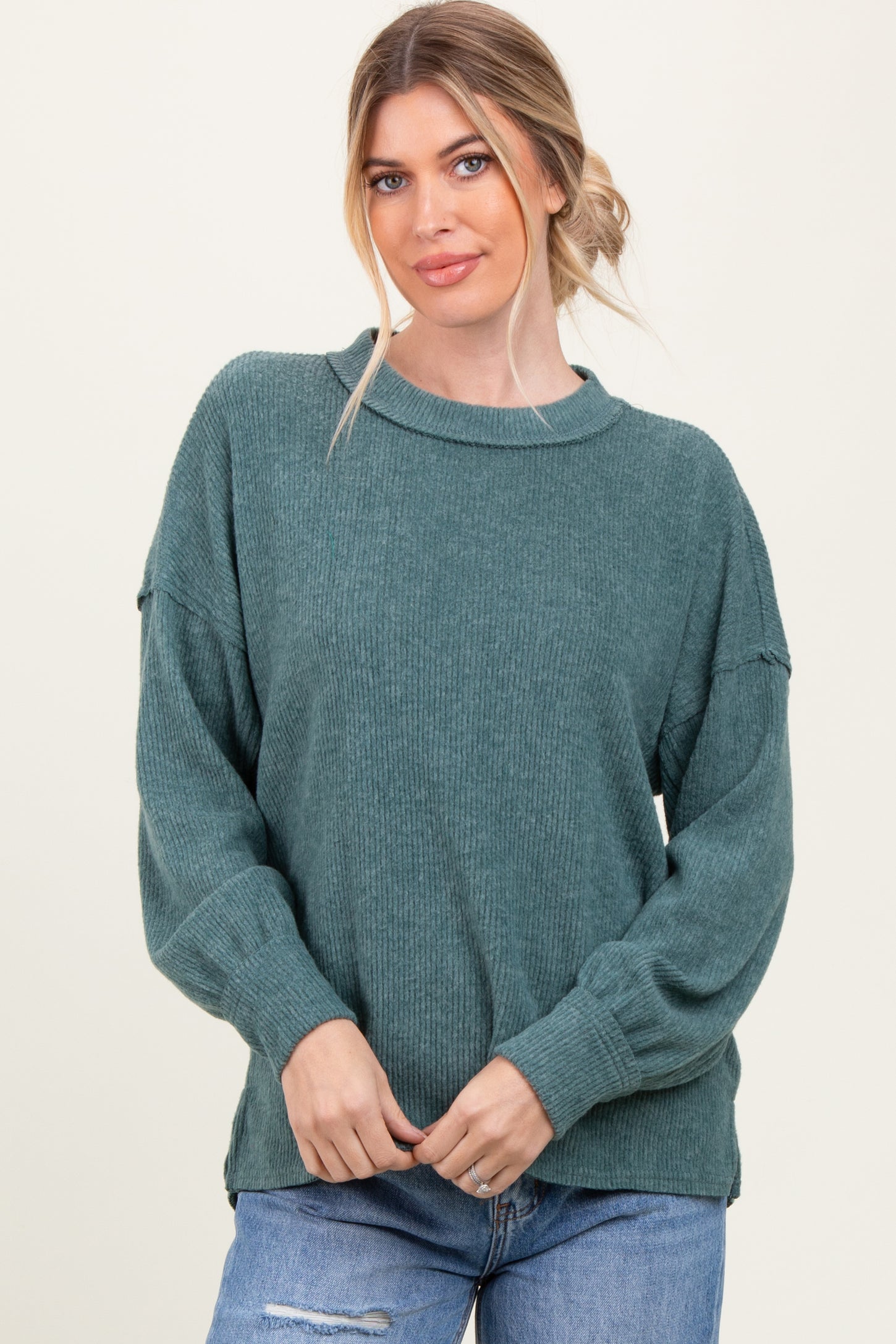 woman wearing a teal ribbed long sleeve sweater with a relaxed fit and side slits, styled with blue jeans