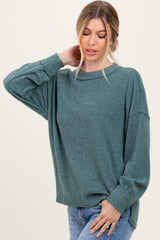 woman wearing a green ribbed oversized sweater and blue jeans, posing with one hand on her neck